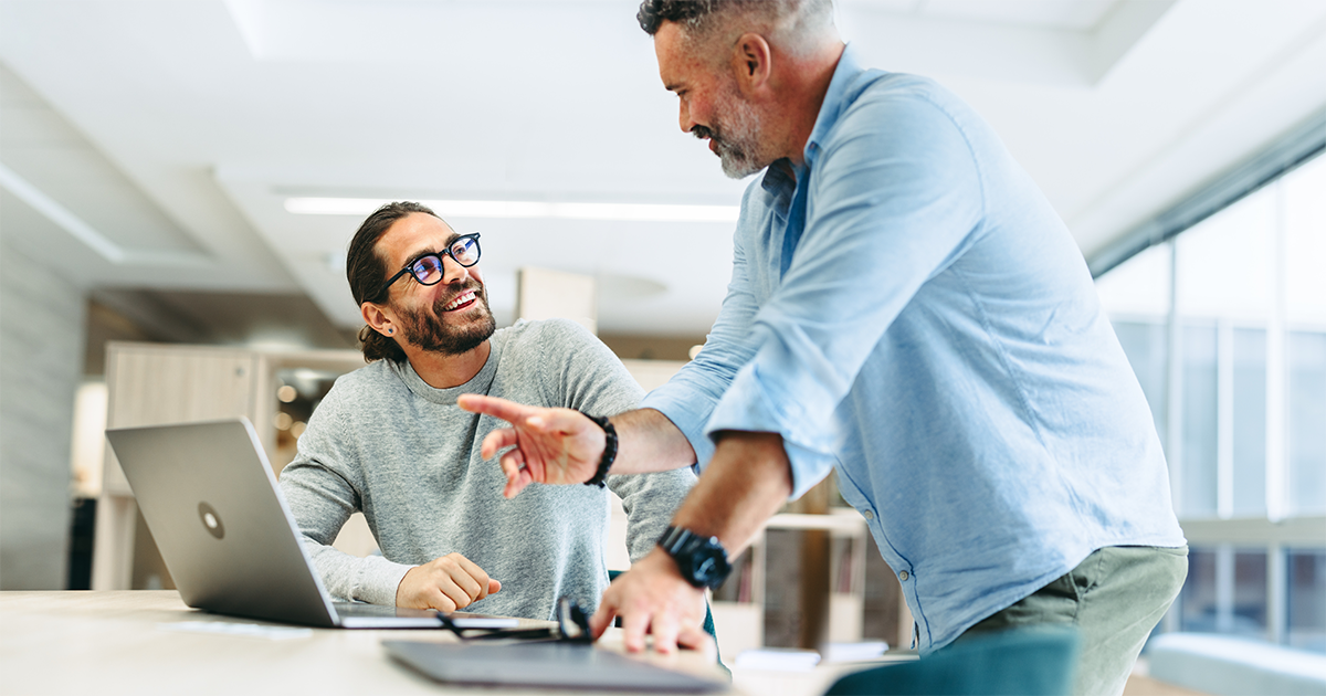 Two business men collaborating and smiling while working on a laptop